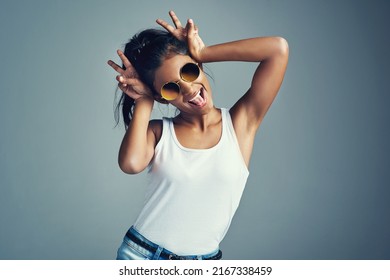 Showing Off Her Quirky Side. Studio Portrait Of A Beautiful Young Woman Gesturing With Bunny Ears Against A Grey Background.