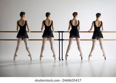 Showing precision. Young girls, ballet dancers in black costumes standing at barre, practicing moves against grey studio background. Concept of ballet, art, dance studio, classical style, youth - Powered by Shutterstock