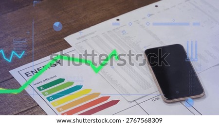 Showing printed documents featuring ENERGY chart, three-hole paper and smartphone on wooden desk. Bargraph, graph, dashboard, data, overlay, analytics, office