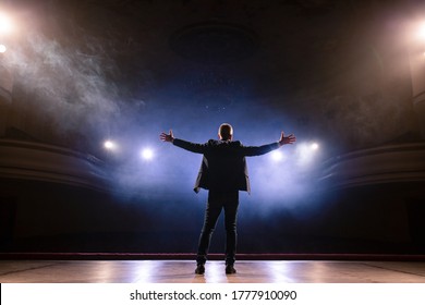 Showman. Middle Age Male entertainer, presenter or actor on stage. Arms to sides, smoke on background of spotlight. Rear view portrait of a male public speaker speaking at the microphone, pointing - Powered by Shutterstock