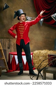Showman. Vintage portrait of male retro circus entertainer expresses rejoice and announces start of show over dark retro circus backstage background. Concept of emotions, art, fashion, style - Shutterstock ID 2258571033