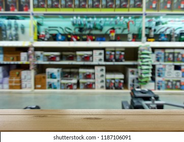 Showroom, Store For Sale Of Equipment For Car Service. Defocused Image Of The Department Of Jacks, Pumps, Fire Extinguishers, Compressors. In The Foreground Is The Top Of A Wooden Table, Counter.