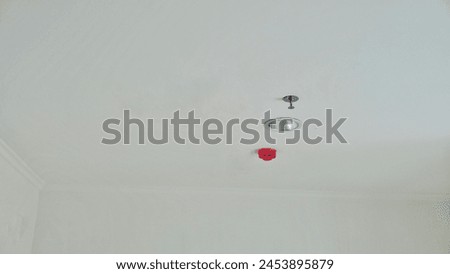 It shows a plain white ceiling equipped with a red fire alarm, springkler and a round light fixture.