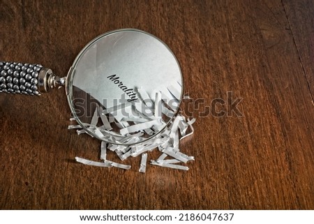 Shred of Morality concept divulging the word ‘Morality’ recovered from a pile of strip-cut shredded paper under a hand-held magnifying glass. 