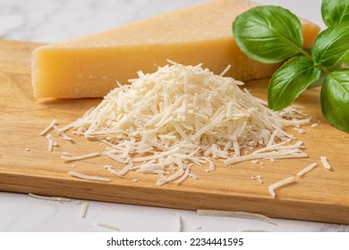 Shredded grana padano cheese on a cutting board. Italian parmesan cheese whole wedge and grated with green basil herb over wooden background. Delicious hard cheese. Dairy product. Front view. - Shutterstock ID 2234441595