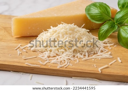 Shredded grana padano cheese on a cutting board. Italian parmesan cheese whole wedge and grated with green basil herb over wooden background. Delicious hard cheese. Dairy product. Front view.