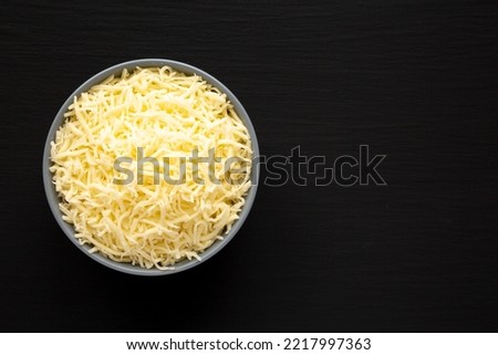Shredded Mozzarella Cheese in a Bowl on a black surface, top view. Flat lay, overhead, from above. Copy space.
