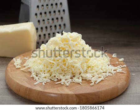Shredded mozzarella cheese on wooden cutting board and shredder