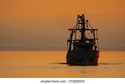 Shrimp Boat At Sunset Silhouetted Against Sunset Sky In Florida