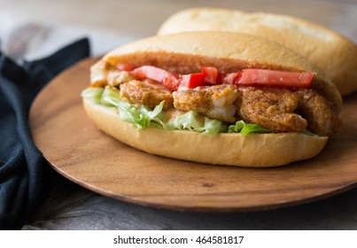 Shrimp po boy sandwich with tomato, lettuce and remoulade sauce on a wooden plate. 