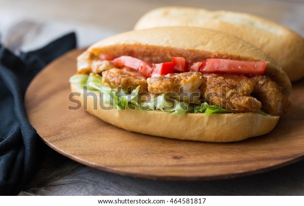 Shrimp po boy sandwich with tomato,\
lettuce and remoulade sauce on a wooden plate.\
