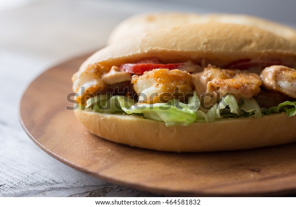 Shrimp po boy sandwich with tomato,\
lettuce and remoulade sauce on a wooden plate.\
