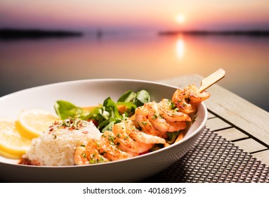 Shrimp with rice and salad in front of a sunset at sea