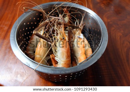 Shrimp in a stainless steel container on a wooden table prepared for serving.