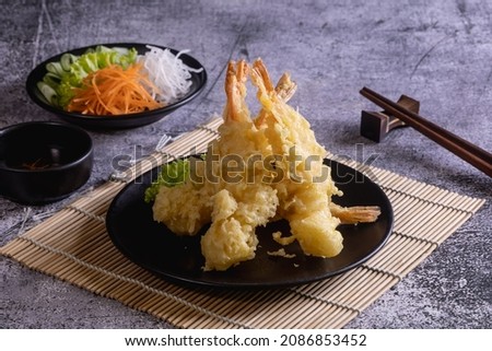 Shrimp tempura in black plate with vegetables and dipping sauce