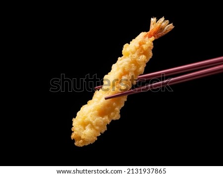 Shrimp tempura lifted with chopsticks against a black background. Tempura is a Japanese food. This is Japanese fried shrimp.