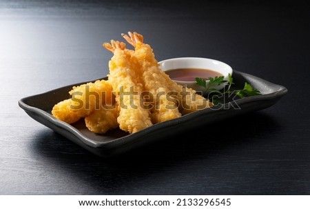 Shrimp tempura on a plate placed against a black background. Tempura is a Japanese food. It is Japanese fried shrimp.