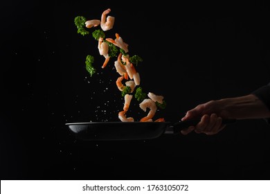 Shrimps With Parsley Frying In A Pan, The Chef Cooks, Freezing In Motion On A Black Background, Healthy And Tasty Food