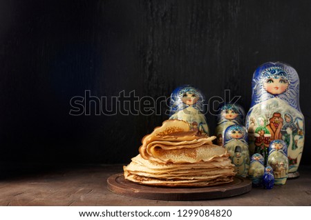Shrovetide Maslenitsa Butter Week festival meal. Stack of russian pancakes blini and traditional wooden dolls matrioshka. Rustic style, close up view with copy space