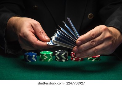 Shuffling of playing cards by the hands of a croupier or a dealer in a poker club. Casino game concept on green table with playing chips. - Shutterstock ID 2247738927