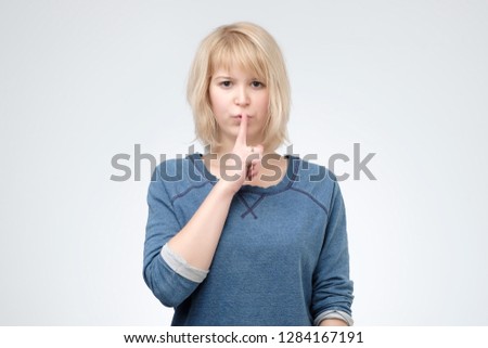 Shush, be silent please. Serious lovely female asks to keep secret information confidential, dressed in blue pulover. Conspiracy concept