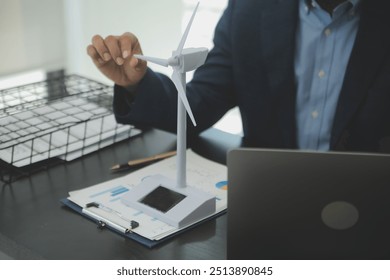 Shut of handsome business man working on new alternative energy development looking at a model of a wind turbine in modern startup. - Powered by Shutterstock