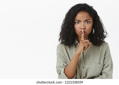 Shut Up And Listen. Portrait Of Intense Displeased Serious-looking African American Woman Shushing At Camera With Dissatisfied Irritated Look Prohibiting Talk Or Tell Anyone Her Secret Over Gray Wall