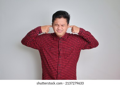 Shut Up ! Portrait Of Unpleasant Asian Man In Casual Plaid Shirt Closing Eyes, Shut Ears With Fingers 