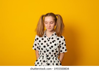 Shy Child Girl With Two Ponytails On A Yellow Background. Teenage Girl Is Shy About Her Hairstyle. 