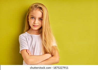 Shy Confident Caucasian Child Girl Isolated Over Green Studio Background, Beautiful Kid Girl With Long Blond Hair Look At Camera Posing, Serious