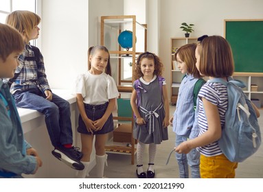 Shy Elementary School Children Meet Each Other For The First Time. Group Of Kids With School Bags Standing In Classroom And Talking. Cute Little Boys And Girls Meet And Make New Friends At School