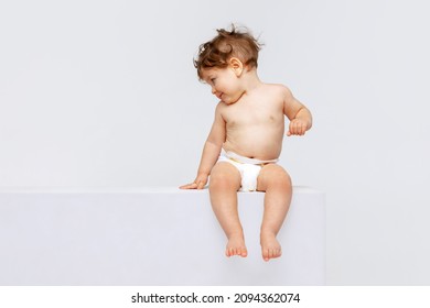 Un niño feliz. Retrato de un niño pequeño y lindo, bebé en pañal sentado tranquilamente y riendo aislado sobre el fondo blanco del estudio. Concepto de infancia, maternidad, vida, nacimiento. Copiar espacio para el anuncio