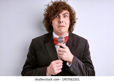 Shy Male Public Speaker With Microphone Isolated On White Background. Curly Guy Is Afraid Of Giving Speech For Crowd Of People Or Audience