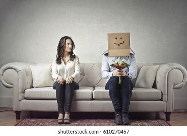 Shy Man Sitting Next To A Woman With His Head Covered By A Cardboard Box