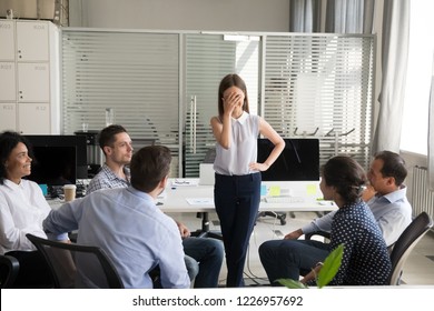 Shy nervous bashful female employee feels embarrassed blushing afraid of public speaking at corporate group team meeting, timid stressed woman hiding face during awkward moment reporting in office