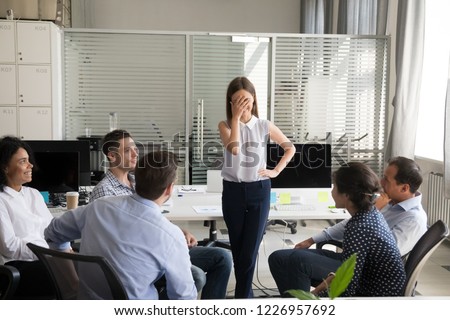 Shy nervous bashful female employee feels embarrassed blushing afraid of public speaking at corporate group team meeting, timid stressed woman hiding face during awkward moment reporting in office Foto d'archivio © 