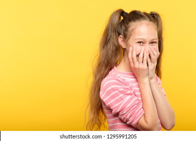 Shy Smiling Embarrassed Girl Covering Mouth With Hands. Young Cute Child Emotional Portrait On Yellow Background.