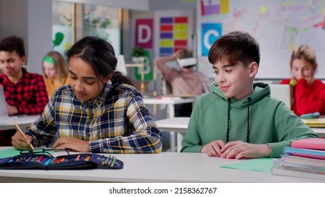 Shy Teen Boy Looking At Classmate . Teen Girl And Boy Sitting Together At Desk In Classroom At School