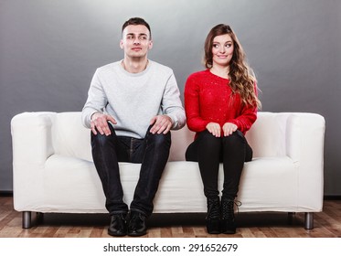 Shy woman and man sitting on sofa couch next each other. First date. Attractive girl and handsome guy meeting dating and trying to talk.