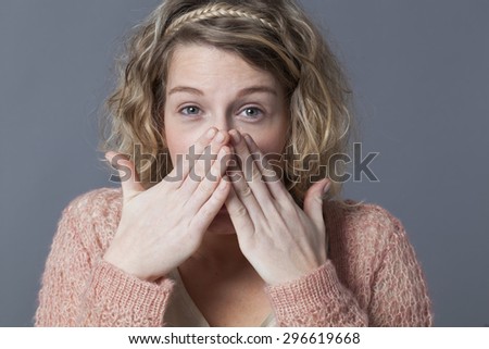 shy young blond woman with curly hair laughing behind her hands for fun and shyness
