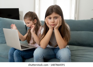 Sibling Angry At Younger Sister Spending Too Much Time Online Using Laptop. Digital Technology Addicted Kid Playing With Computer Ignoring Her Sad Older Sister. In Children And Internet Addiction.