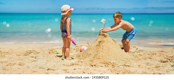 Sibling boy building a sandcastle at the beach in summer