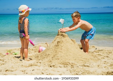 Sibling boy building a sandcastle at the beach in summer