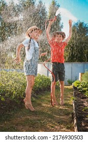 Sibling Children Frolic Splashing With A Water Hose In The Backyard In The Garden On Summer Holidays In The Village On A Hot Day. Friends Fun