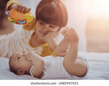 Siblings, baby and playing with toy on bed for bonding, fun activity and motor skills development in home. Family, brothers and curious child with plastic rattle for entertainment and love in bedroom - Powered by Shutterstock