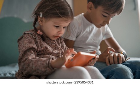 Siblings brother boy hold smartphone with girl sister children use mobile phone smartphone at home in room watch video make a call or play online games leisure family concept real people copy space - Shutterstock ID 2395054031
