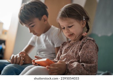 Siblings brother boy hold smartphone with girl sister children use mobile phone smartphone at home in room watch video make a call or play online games leisure family concept real people copy space - Shutterstock ID 2395054033