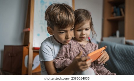 Siblings brother boy hold smartphone with girl sister children use mobile phone smartphone at home in room watch video make a call or play online games leisure family concept real people copy space - Shutterstock ID 2395054035