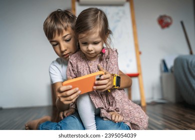 Siblings brother boy hold smartphone with girl sister children use mobile phone smartphone at home in room watch video make a call or play online games leisure family concept real people copy space - Shutterstock ID 2395054039