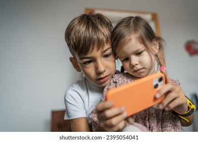 Siblings brother boy hold smartphone with girl sister children use mobile phone smartphone at home in room watch video make a call or play online games leisure family concept real people copy space - Shutterstock ID 2395054041